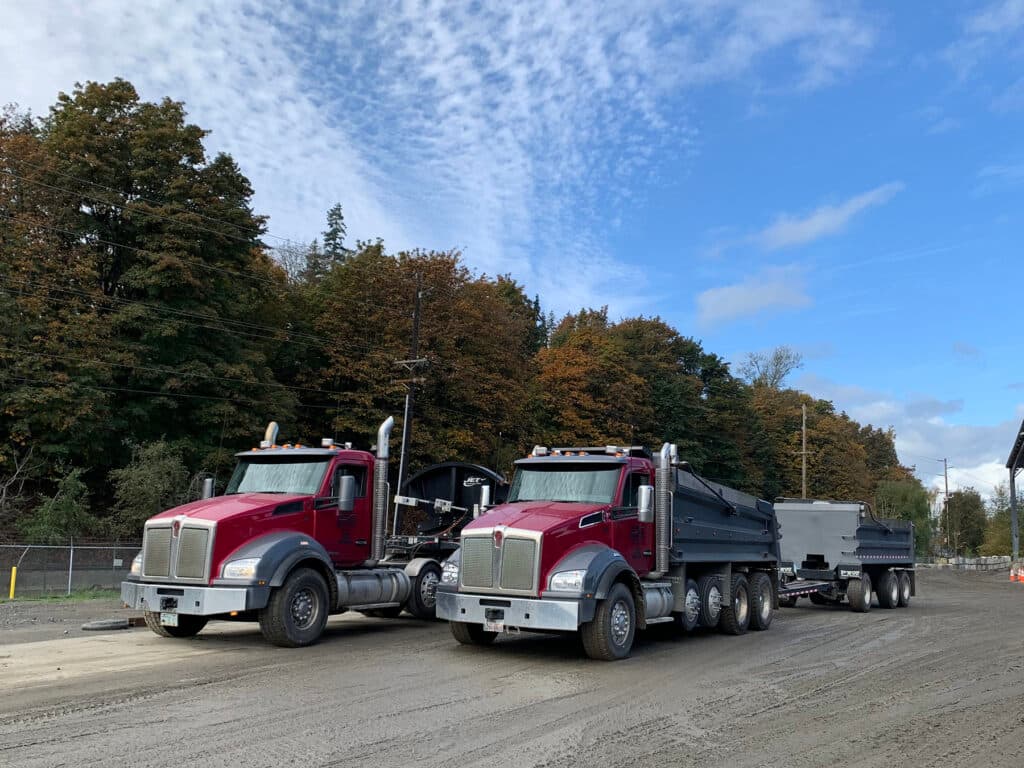 Two of the red DC Materials dump trucks parked side by side in the yard